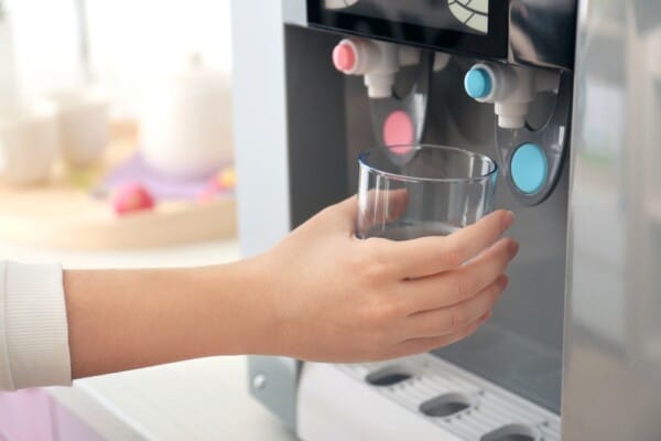An employee fills up a glass with cold water from an office water dispenser
