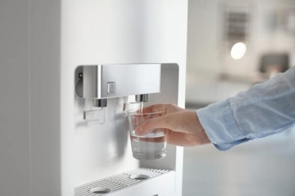 A woman fills a glass using a plumbed-in water cooler